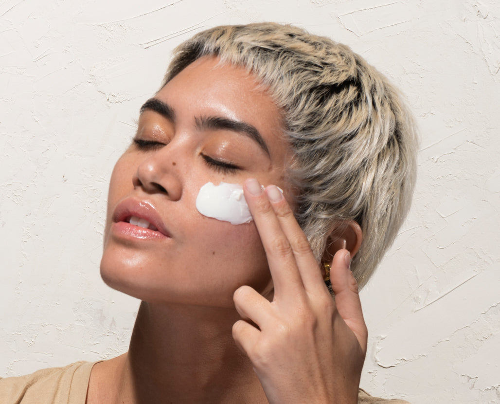 Woman applying cream to her face against a light background